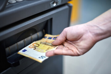 Hand retrieves euro banknotes from ATM. Rising prices, inflation, economic crisis, decreasing...