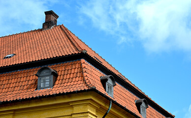 Vibrant architectural detail of a historic European house with striking red roof tiles and ornate stone decoration. The enhanced colors and contrast highlight the vivid textures and classic design