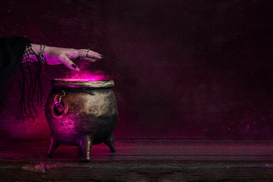 Witch's hand over a cauldron with a magic potion in a dark room. Witch casting spells on Halloween night