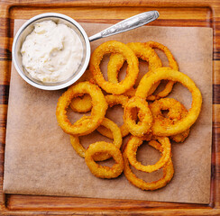 Crispy onion rings served with dipping sauce on a wooden tray