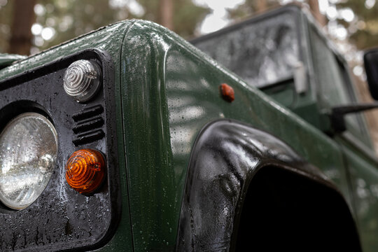 Green 4x4 vehicle front quarter panel and headlight with forest background - Powered by Adobe