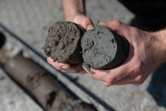 Hands holding two soil core samples in laboratory setting during environmental research analysis procedure