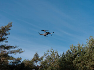Modern quadcopter drone in flight against clear blue sky during professional aerial survey or photography mission