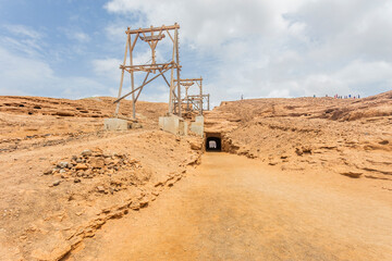 Colorful daytime photograph of traditional salt flats on Sal Island, Cape Verde. Outdoor landscape showcasing vibrant salt pans and distant silhouettes of unidentified people in the background. Captur