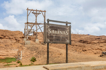 Colorful daytime photograph of traditional salt flats on Sal Island, Cape Verde. Outdoor landscape showcasing vibrant salt pans and distant silhouettes of unidentified people in the background. Captur