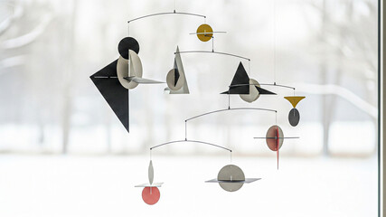 An artistic mobile sculpture hangs gracefully in front of a window, creating a modern and elegant scene. The sculpture features a balance of shapes and colors