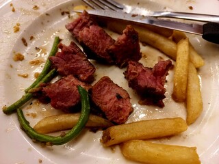 Delicious beef steak pieces with vegetables and potatoes being eaten on a plate