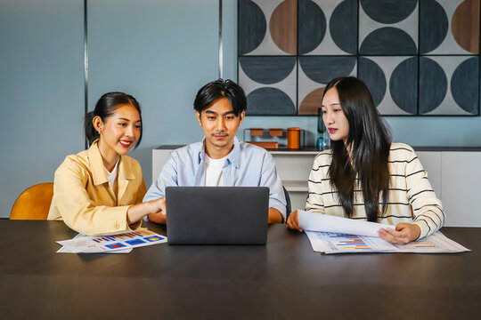 Three asian individuals engage in a serious discussion at a table. Each person reviews graphs and statistics displayed on laptop computer, collaboratively analyzing data with focus and intent.