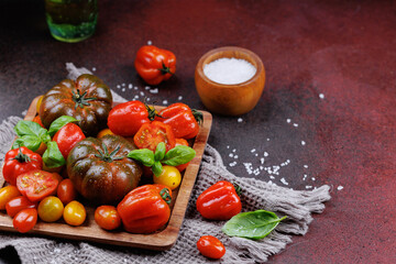 Heirloom tomatoes and fresh basil with sea salt on red rustic table and textured fabric, highlighting healthy and seasonal plant-based food