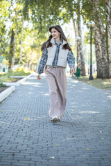 Obraz premium Full-length portrait of a young beautiful girl in a checkered shirt and beige pants