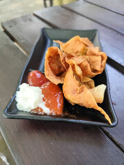 Four crispy, golden brown fried dimsums, served on a black plate with two dipping sauces (red chili sauce and white mayonnaise) on the side.