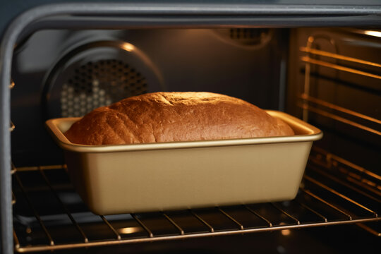 A close-up photograph of a golden-brown loaf of bread baking in a rectangular ceramic baking pan inside an oven.