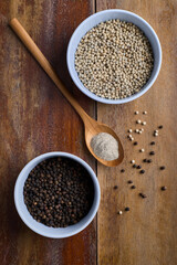 Black and white pepper in a light blue cup and wooden spoon on an old wooden table.