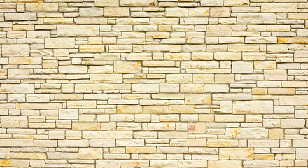 Fototapeta premium Seamless textured background of a light beige and cream colored stacked stone wall with irregular rectangular blocks and natural variations