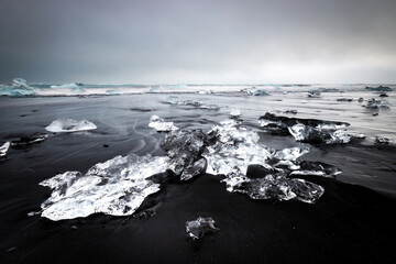 Obraz premium Long exposure of crystal-clear chunks of ice lying on Diamond Beach black sand of Iceland’s coast near Jökulsárlón, creating a striking contrast in color and texture