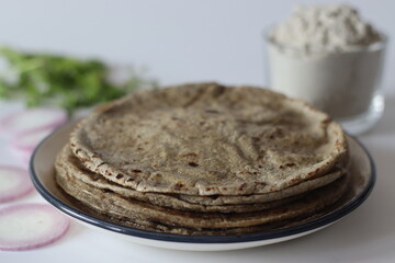 Bajra roti on plate with bajra atta, onion slices, and herbs staple Indian food evoking tradition