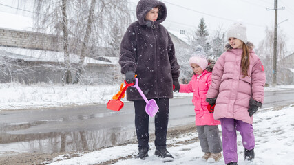 Grandmother and girls walk along a snowy street in winter