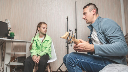 Father and daughter playing guitar and learning musical notes at home. Skilled personal tutor teaches his little student to be good at playing guitar.