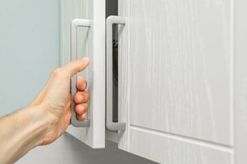 a man's hand opens a kitchen cabinet door. man opens closet, close-up. High quality photo