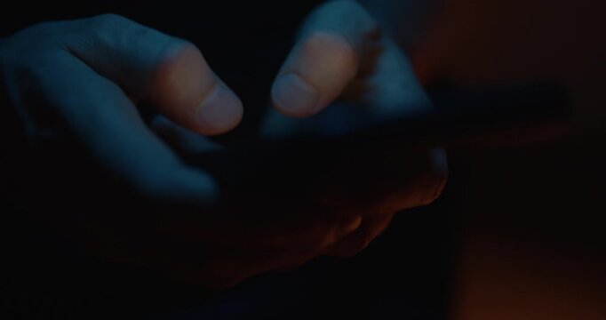 Hands typing at night with phone, texting on the internet in the dark to cyberbullying. Writing comments on social media with a smartphone.