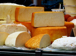 various types of delicious large cut round soft cheese pieces in yellow and white color. open food market with cheese on display. rich food concept. dairy food. food production and agriculture