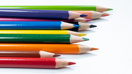 Fototapeta premium A Line of colorful pencils with their tips pointing in the same direction on a clean white background, highlighting a variety of colors.