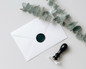 Minimal top view of white envelope with green wax seal and eucalyptus leaf, styled with black stamp on neutral background