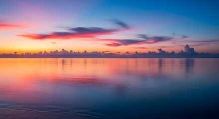 Obraz premium Serene ocean reflecting vibrant sunset colors with clouds on the horizon and smooth water surface view