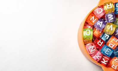 a small orange plastic bowl filled with a random assortment of colorful, translucent alphabet beads on a white surface.