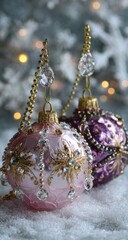 Elegant pink and purple glass ornaments adorned with crystals and gold accents, resting on faux snow