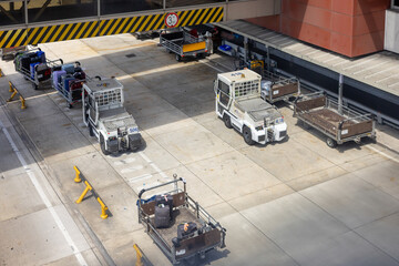 Airport service vehicles with baggage carts parked on the tarmac during luggage handling operations.