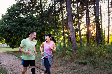 Fototapeta premium Happy diverse middle-aged couple jogging together in park, smiling and talking while exercising outdoors, enjoying active lifestyle, health, and fitness in nature