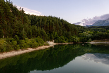 Fototapeta premium A tranquil alpine lake bordered by green forests with the Pirin mountain range in the background, near the resort town of Bansko, Bulgaria. A picturesque nature landscape.