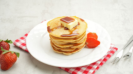 Stack of golden pancakes with strawberries on a white plate, breakfast food
