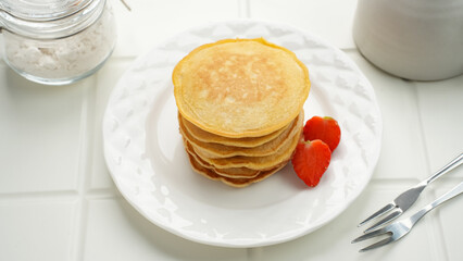 Stack of golden pancakes with strawberries on a white plate, breakfast food
