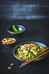 Asian mie noodles with spring onions and sugar peas, topped with cucumber and roasted peanuts