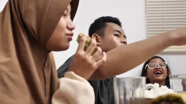 Asian muslim siblings doing chit chat talks while eating dinner, sitting on floor with low dining table