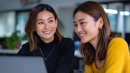 Two young female business professionals engaged in friendly conversation in an office setting.