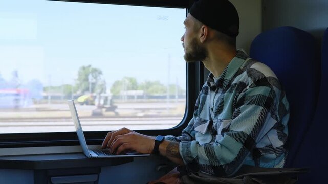 Young man with backpack working on laptop inside train, remote work while traveling by railway. Digital nomad concept