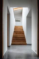 Modern hallway with wooden staircase and skylight, featuring minimalist design and ample natural light.