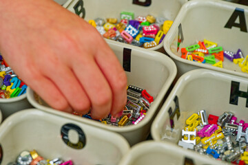 A Hand selecting colorful alphabet beads from organized plastic boxes for crafts with letter I O H