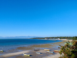 Scenic tropical coastline with colorful fishing boats on the shore during low tide, under clear sunny weather