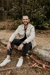Smiling man sitting on a log in the forest wearing casual clothes