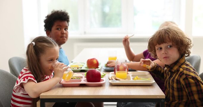 Little kids eating lunch at wooden table in school canteen