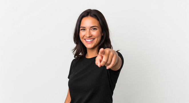 A confident young woman with a warm smile pointing directly at the camera, inviting interaction or selection from the viewer, on a clean white background