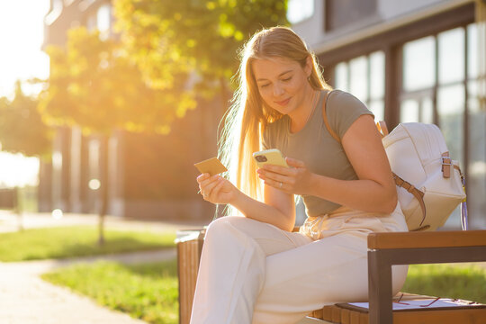 Young woman shopping online using a smartphone and credit card outdoors