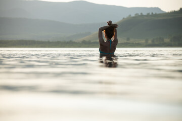 Woman swims in the mountain lake at sunset. Beautiful summer landscape.