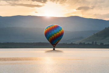 Colorful hot air balloon flying over the lake at sunset. Mountains and sky in the background
