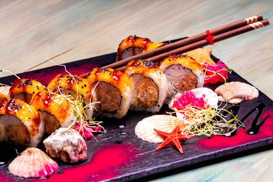 Gourmet Japanese sushi rolls with creamy sauce, sesame and seaweed. A creative dish served on a black slate plate with seashells.