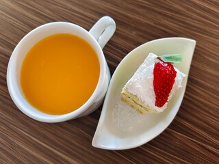 Top view of a cup of orange drink served with a slice of strawberry cake on a wooden table. Delicious dessert and refreshing beverage concept for cafe, restaurant, and food photography